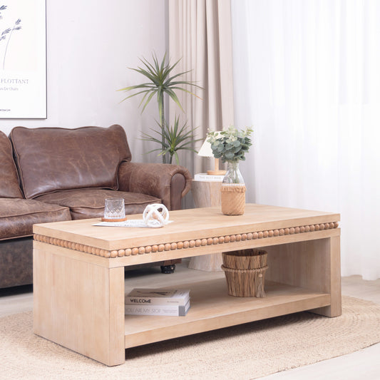 Wood coffee table with open shelf and beaded trim styled in a cozy living room with leather sofa and decorative accents.