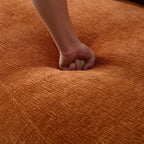 Hand pressing into deep seat of modern L-shape sectional sofa, showcasing the plush and resilient cushion texture in burnt orange fabric.