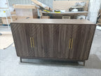 Assembled walnut sideboard with gold handles and geometric door design, displayed in a workshop setting before final placement.