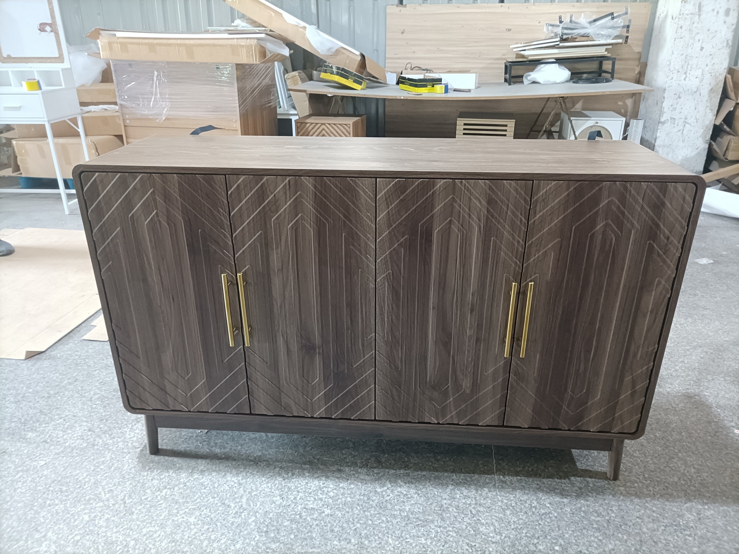 Assembled walnut sideboard with gold handles and geometric door design, displayed in a workshop setting before final placement.