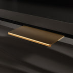 Detail of gold drawer handle on black credenza, highlighting elegant hardware and textured drawer front.