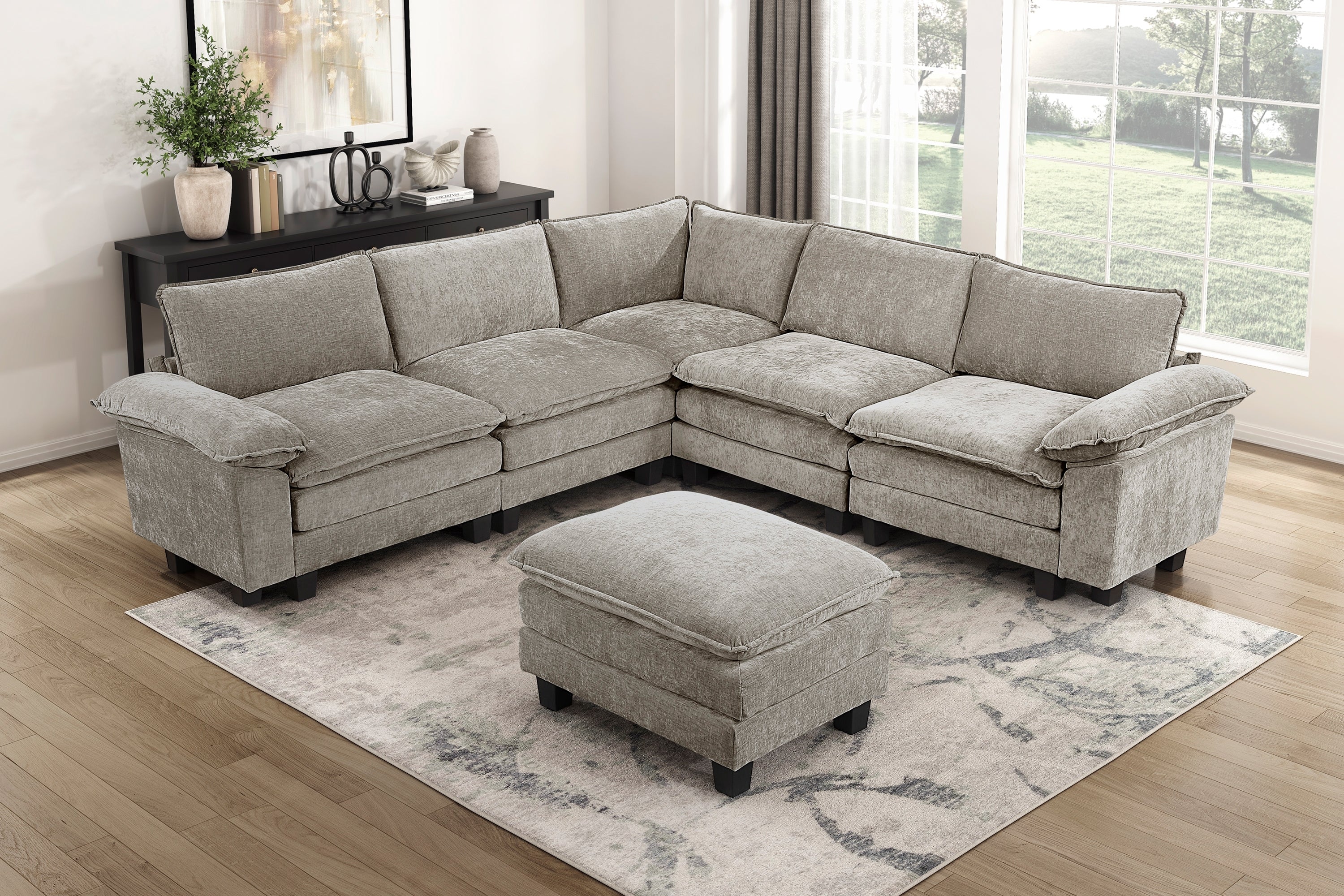 Modern gray modular sectional sofa in plush chenille fabric with a matching ottoman on a patterned area rug.