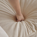 Hand pressing into soft chenille cushion of beige sectional sofa. Demonstrates superior comfort and plush seating experience.