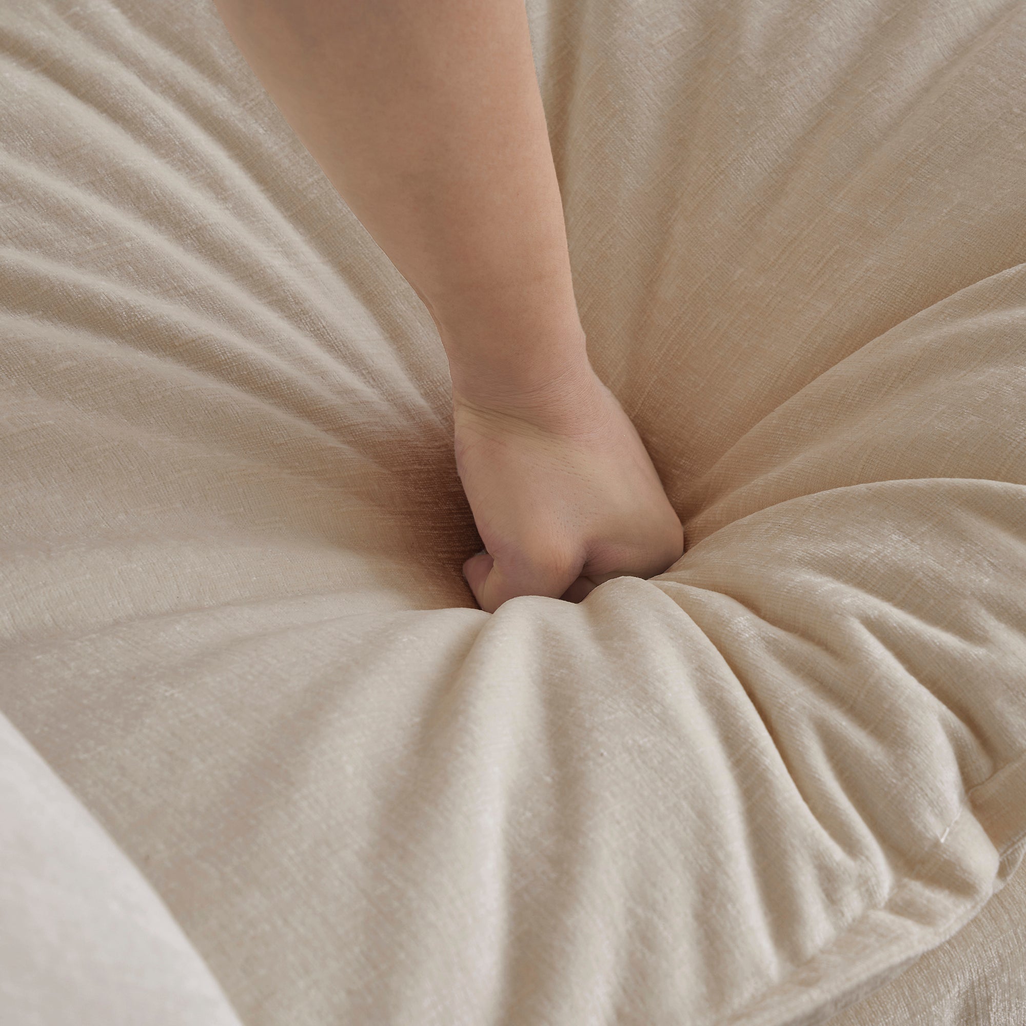 Hand pressing into soft chenille cushion of beige sectional sofa. Demonstrates superior comfort and plush seating experience.
