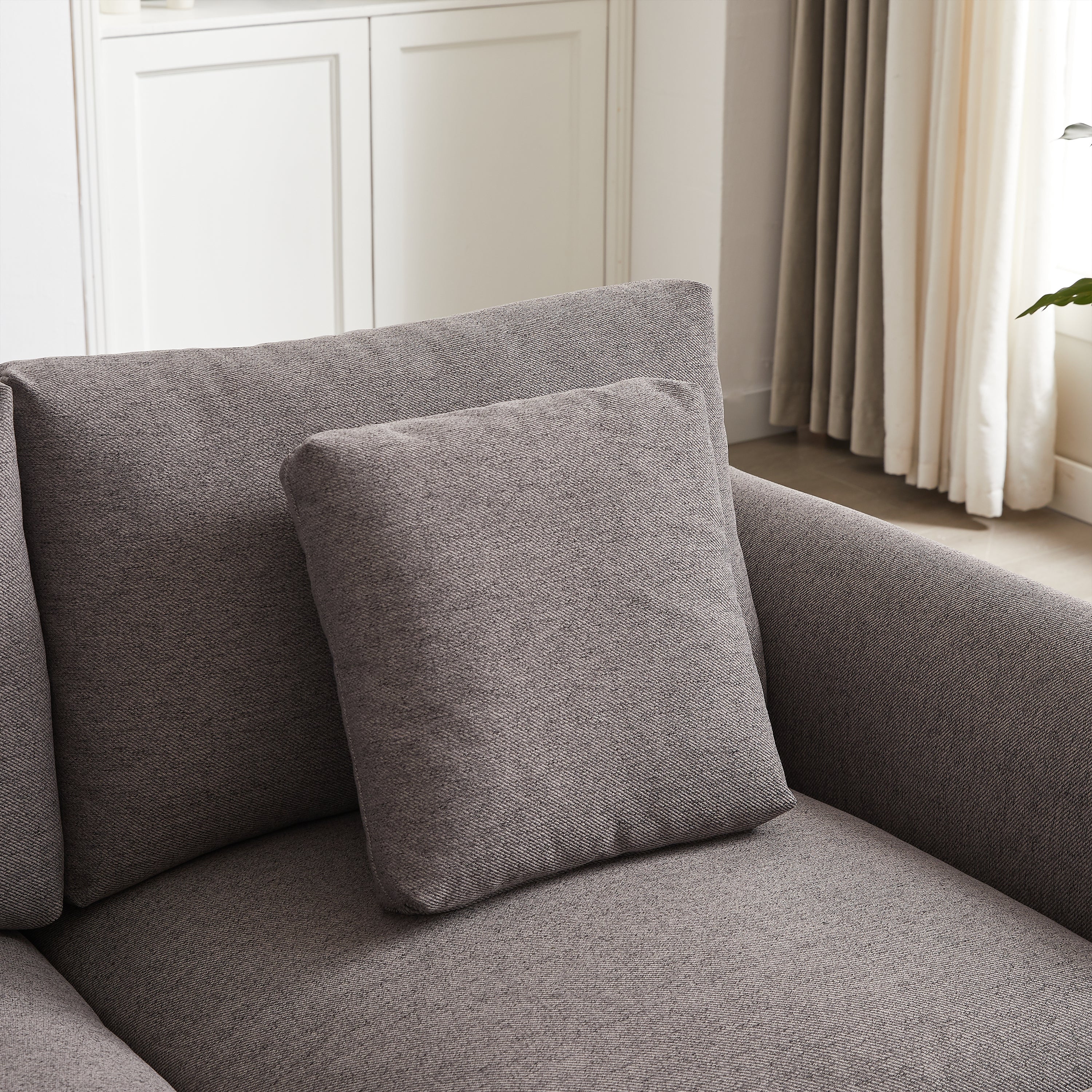 Detail of square throw pillow on gray modular sofa, emphasizing the soft fabric and cohesive design of the upholstered furniture.