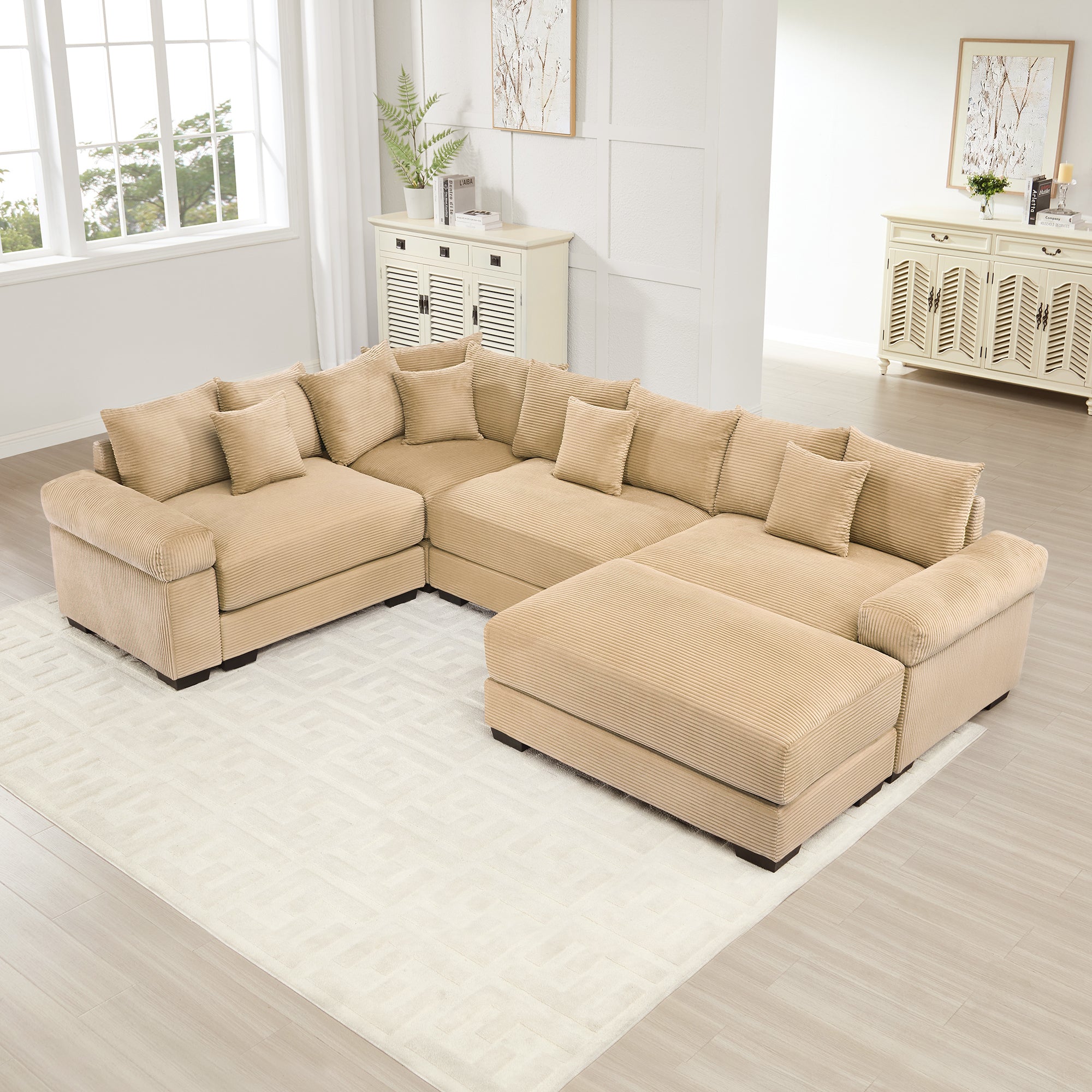 Oversized camel corduroy modular sectional sofa with extra-thick armrests and a matching ottoman in a bright living room.