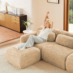 Woman relaxing on light khaki 2-seater modular sofa with plush fabric. Ideal for lounging in a cozy home environment.