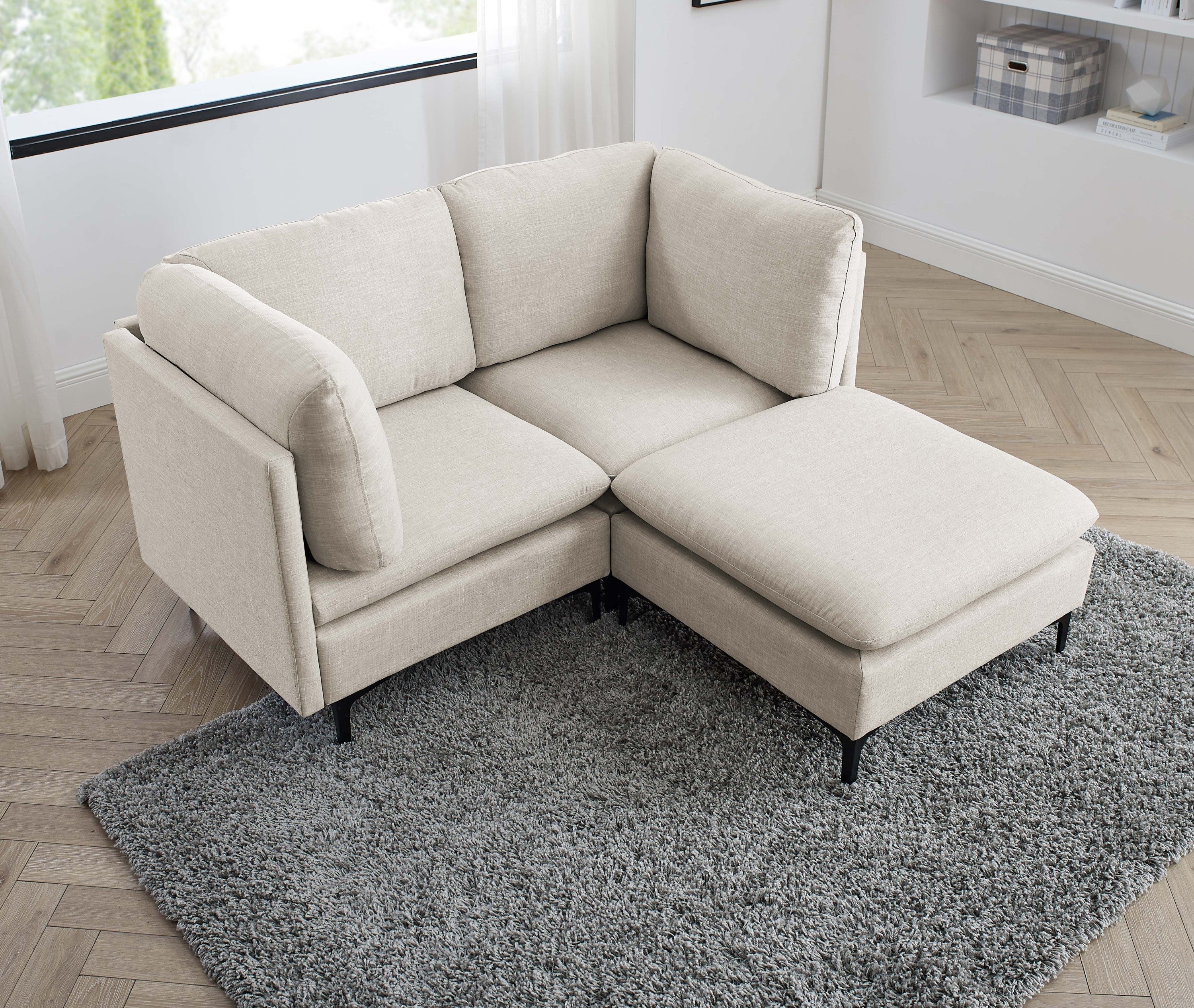 Beige linen modular sectional sofa with plush cushions and black metal legs, set on a gray rug.