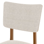 Close-up of upholstered chair backrest from farmhouse dining table set for 4, featuring beige fabric and wooden frame.
