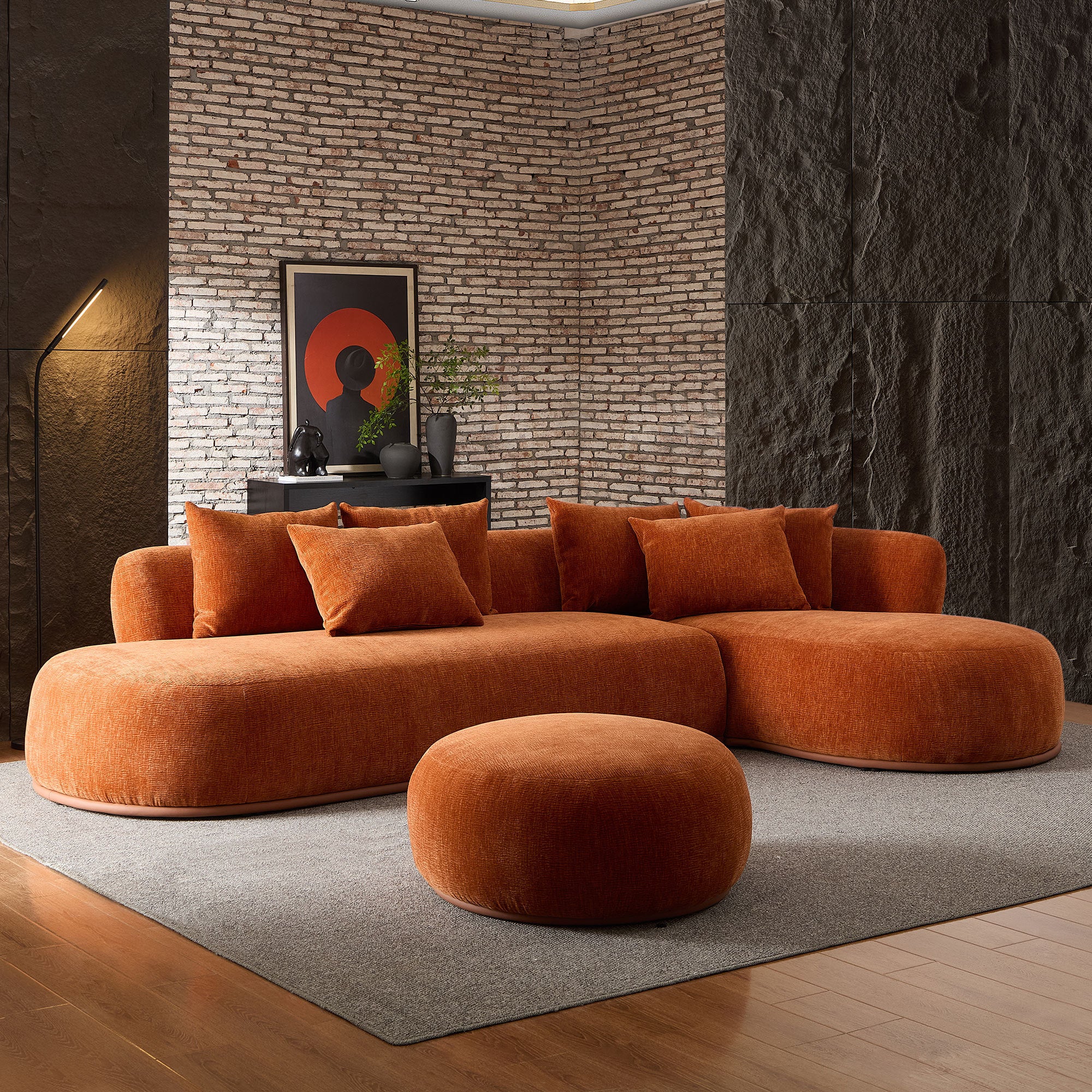Modern orange oversized L-shape sectional sofa with ottoman in a dark-toned room, offering bold style and spacious seating.