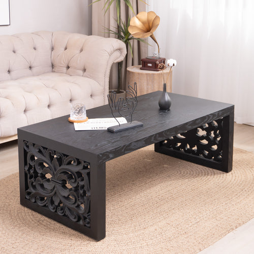Black carved wood coffee table with ornate side panels placed in a cozy living room, adding elegance to the furniture setup.