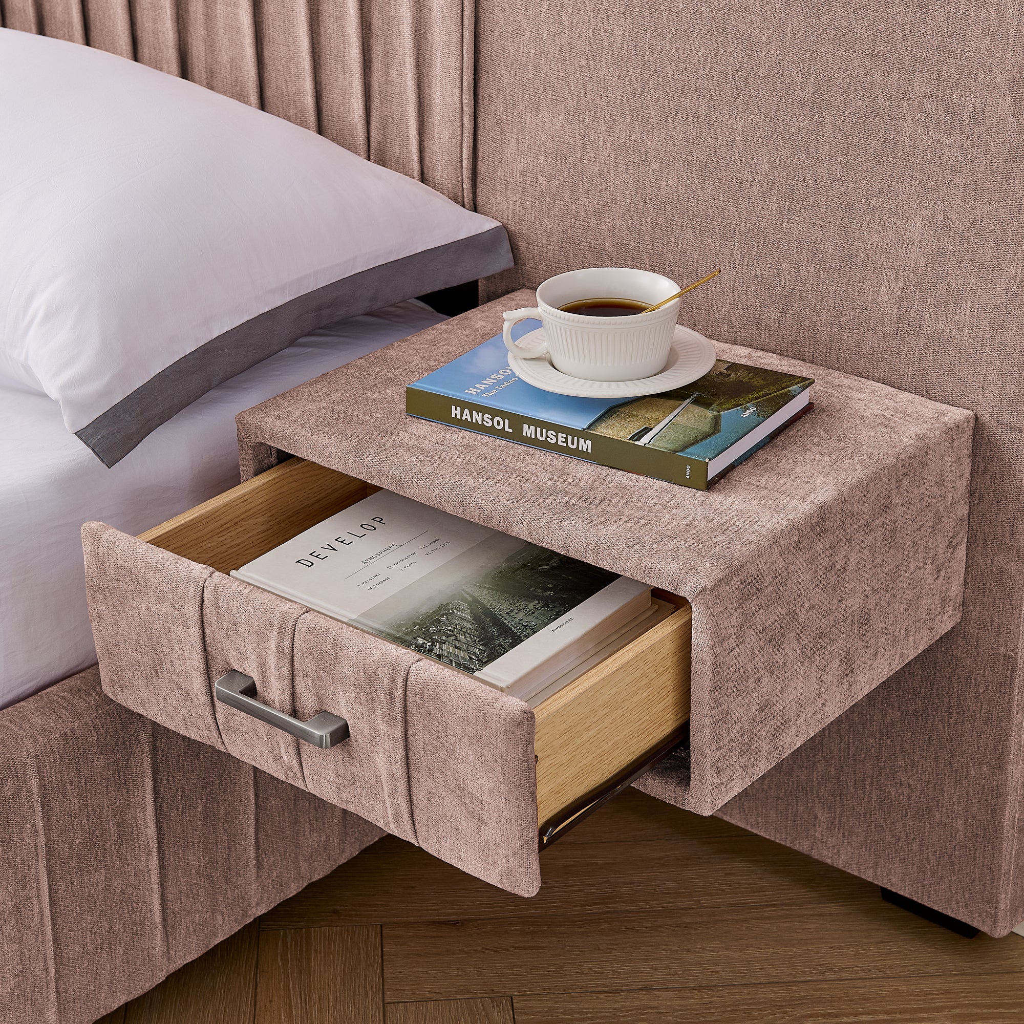 Detail of built-in nightstand drawer on upholstered queen bed, showing storage space with books and coffee cup on top.