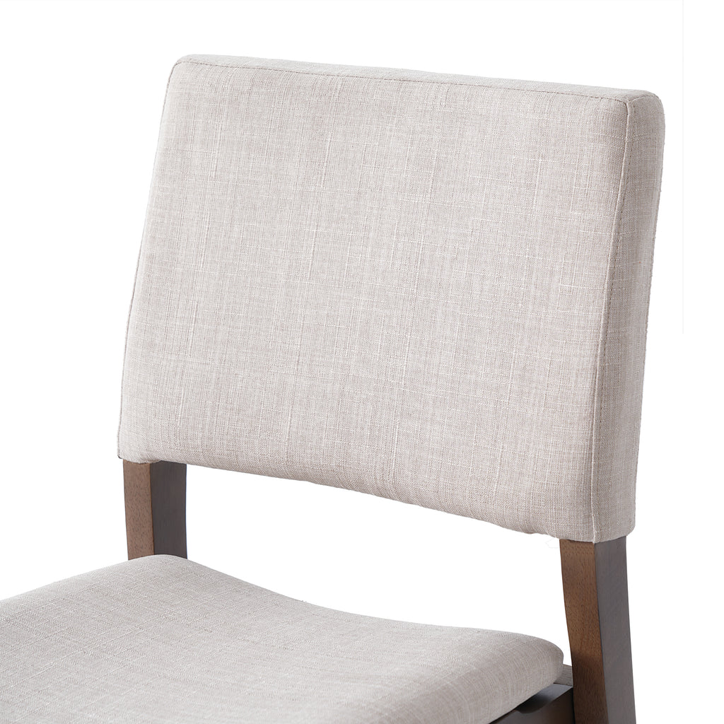 Close-up of the cushioned backrest in beige fabric on a walnut finish dining chair from the Modern Dining Set collection.