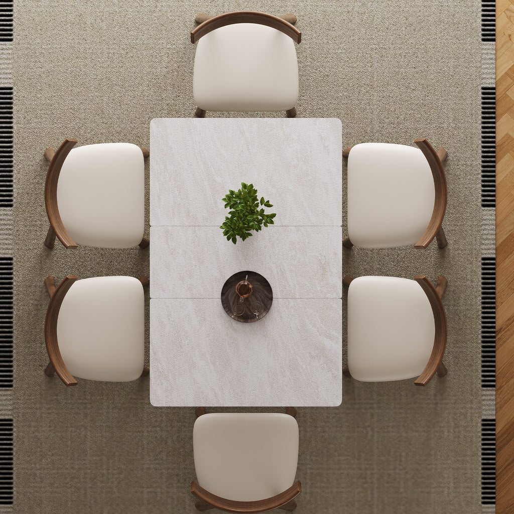 Top view of expandable dining table set with rock slab surface and six cushioned wooden chairs arranged around it on a textured rug.