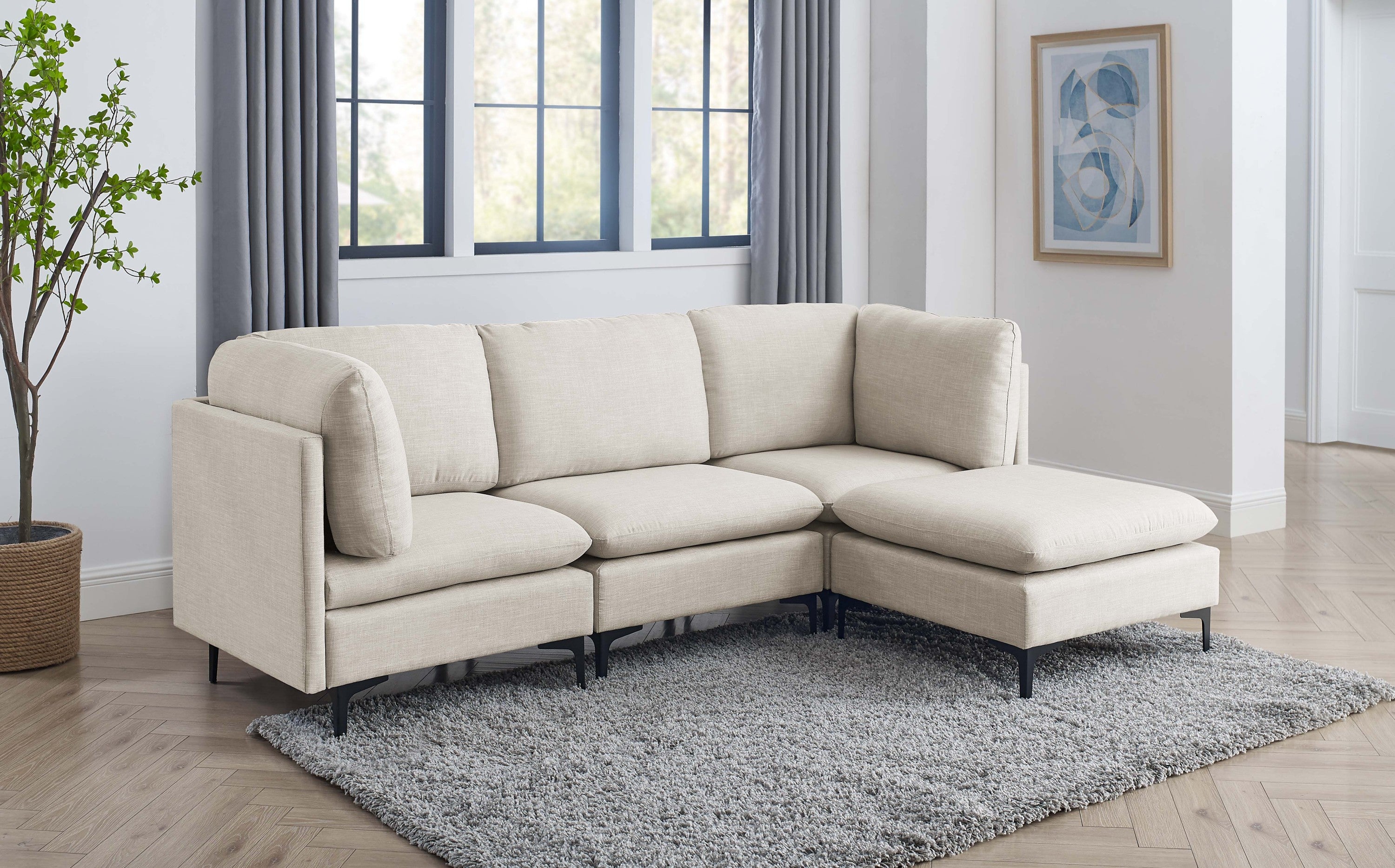 Beige linen modular sectional sofa with plush cushions and sleek black metal legs on a grey area rug in a bright room.