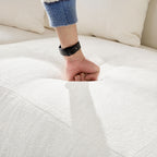 Hand pressing into the seat cushion of the beige sectional sofa, showing the medium-soft density and plush comfort of the seating.