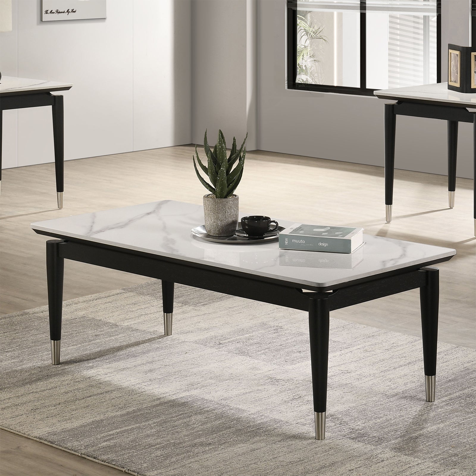 Contemporary coffee table with sintered stone top in black and white, featuring silver-capped tapered legs, styled in a modern living room.