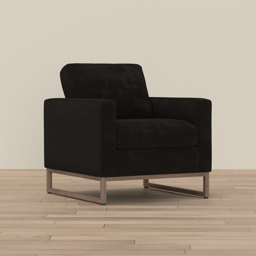 Modern black fabric accent chair with a boxy silhouette and a minimalist wood-tone metal sled base.