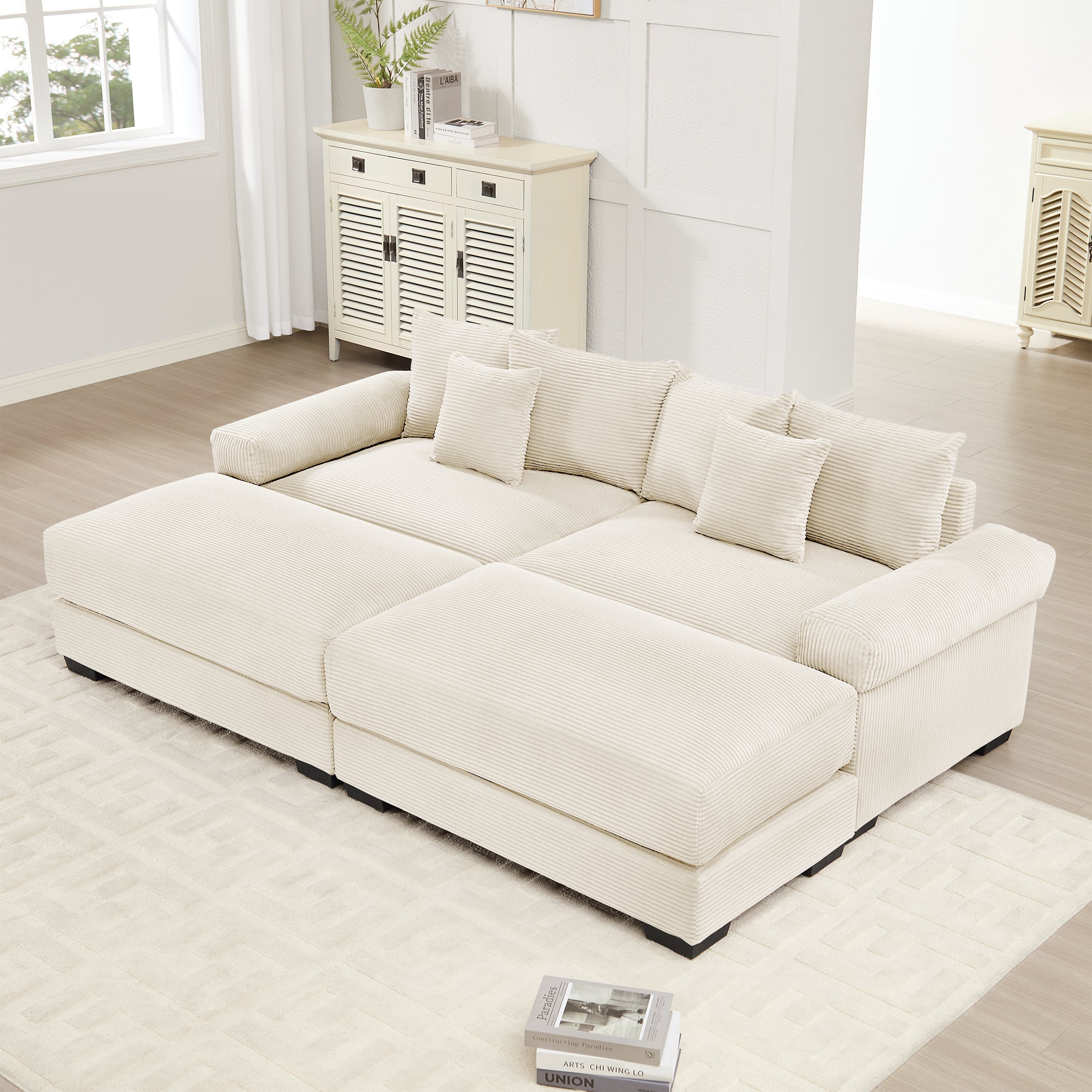 Oversized cream corduroy modular sectional sofa with deep seats, wide armrests, and matching ottoman in a bright room.