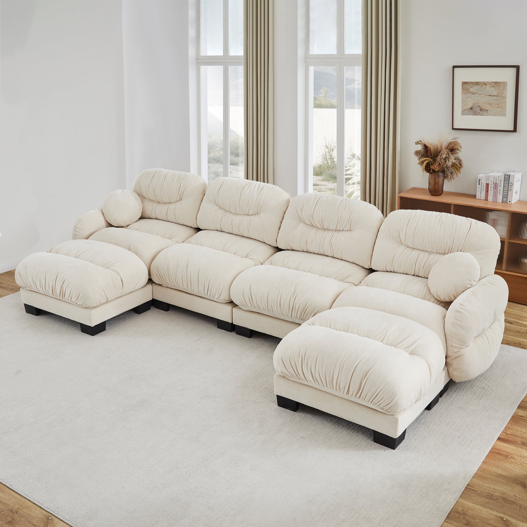 Beige pleated chenille U-shaped sectional with rounded arms, two ottomans, and two round throw pillows on a rug.