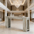 Rustic white-washed wooden console table with wide, open legs, set in a luxurious, grand foyer.
