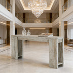 Rustic white-washed wooden console table with wide, open legs, set in a luxurious, grand foyer.