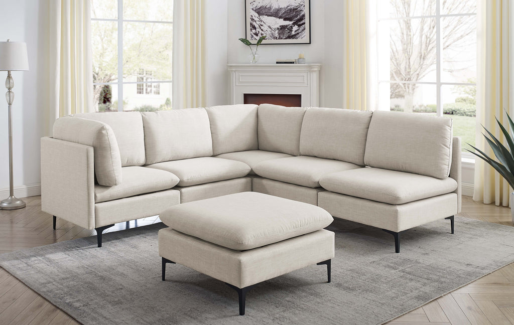 Beige linen modular sectional sofa with matching ottoman and sleek black metal legs in a bright living room.