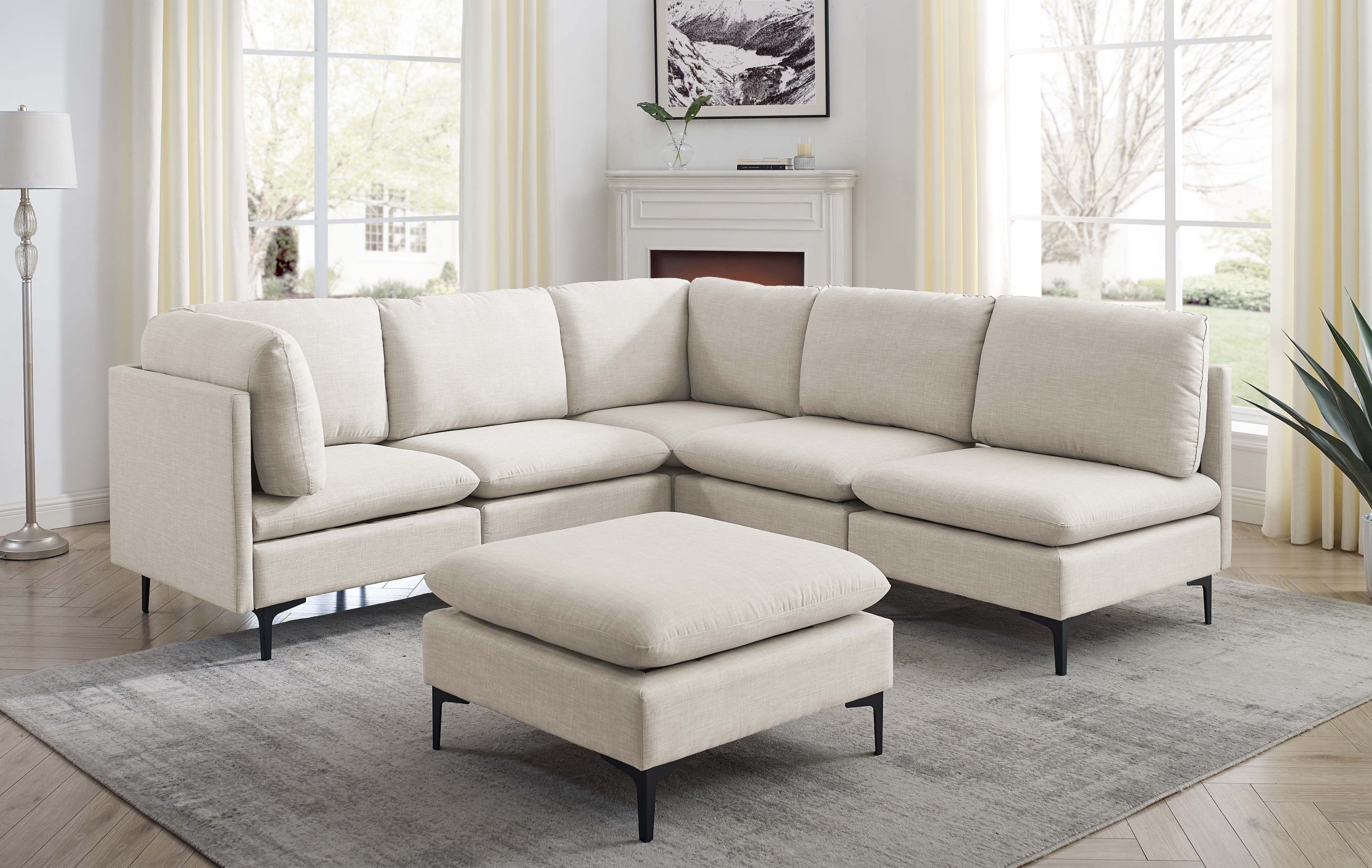 Beige linen modular sectional sofa with matching ottoman and sleek black metal legs in a bright living room.