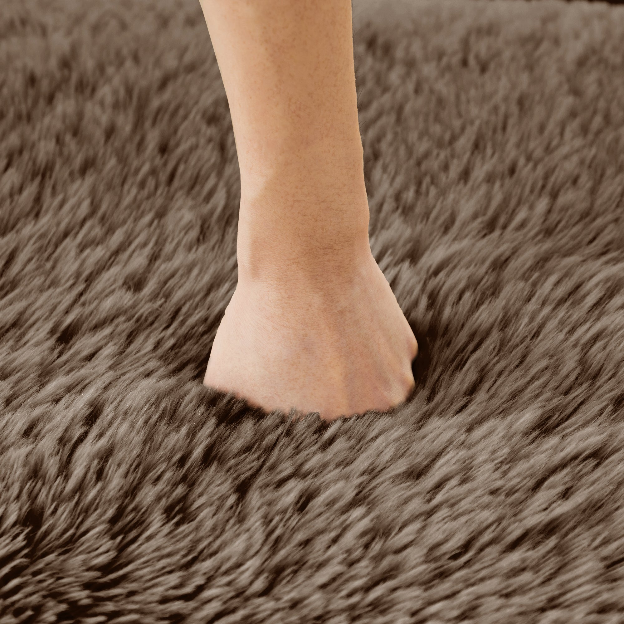 Hand pressing into chocolate plush fabric of modular sofa, demonstrating soft, high-density cushioning and premium texture.
