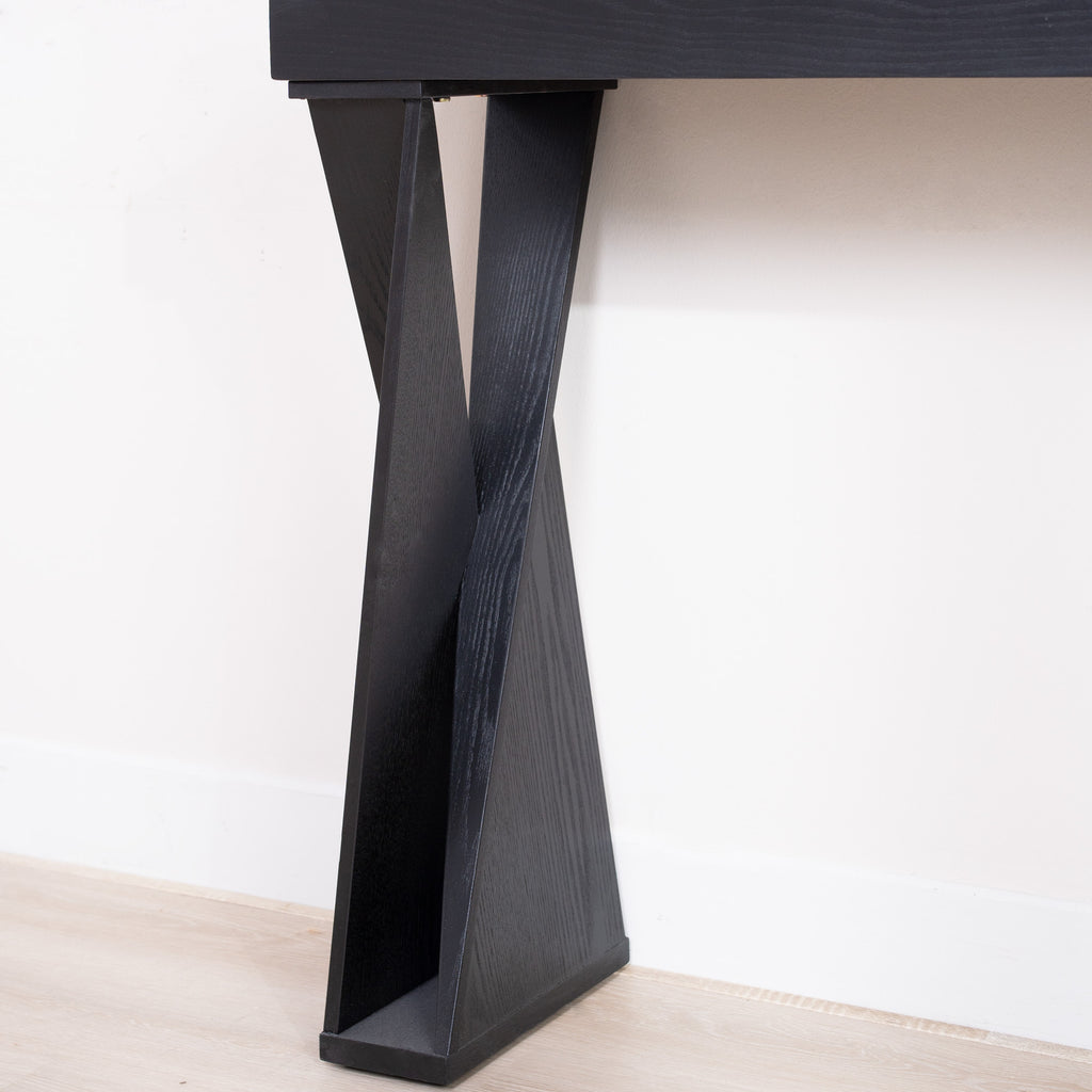 Close-up of the base of a black console table with crossed legs, highlighting the angular design and wood texture.