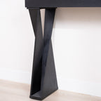 Close-up of the base of a black console table with crossed legs, highlighting the angular design and wood texture.