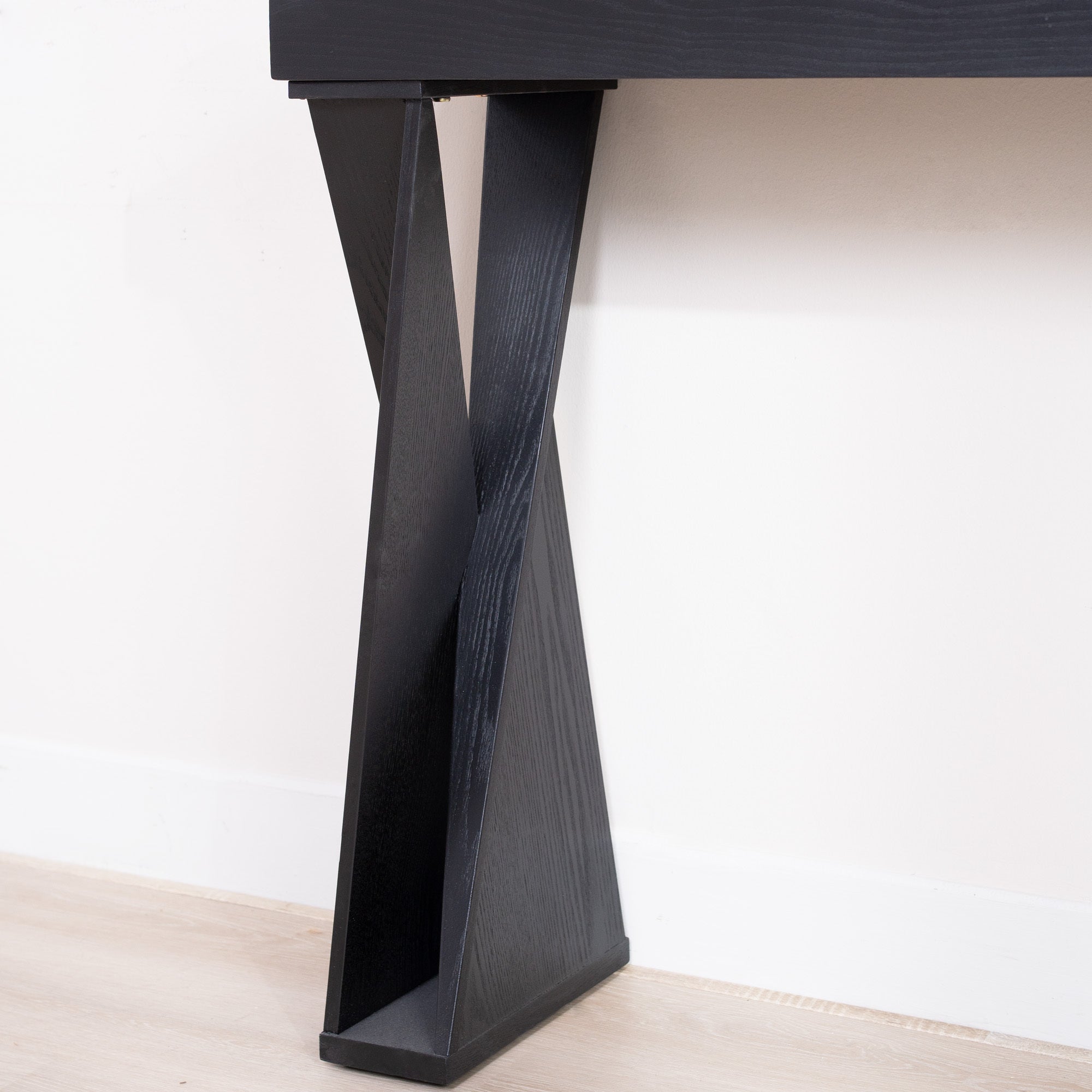 Close-up of the base of a black console table with crossed legs, highlighting the angular design and wood texture.
