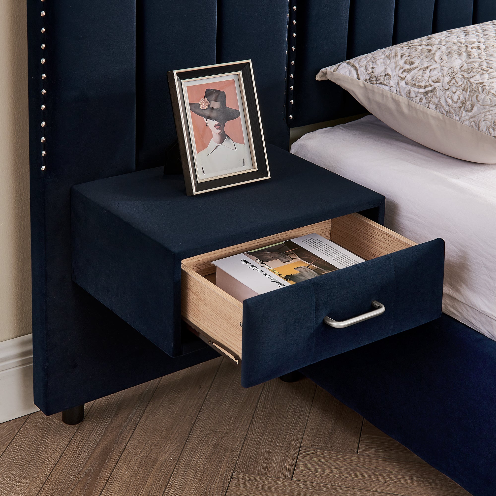 Open drawer of built-in nightstand on queen velvet bed frame showing storage space and modern handle design.