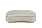 Curved beige tight-back sofa with brown piping detail on a light wood plinth base against a white background.