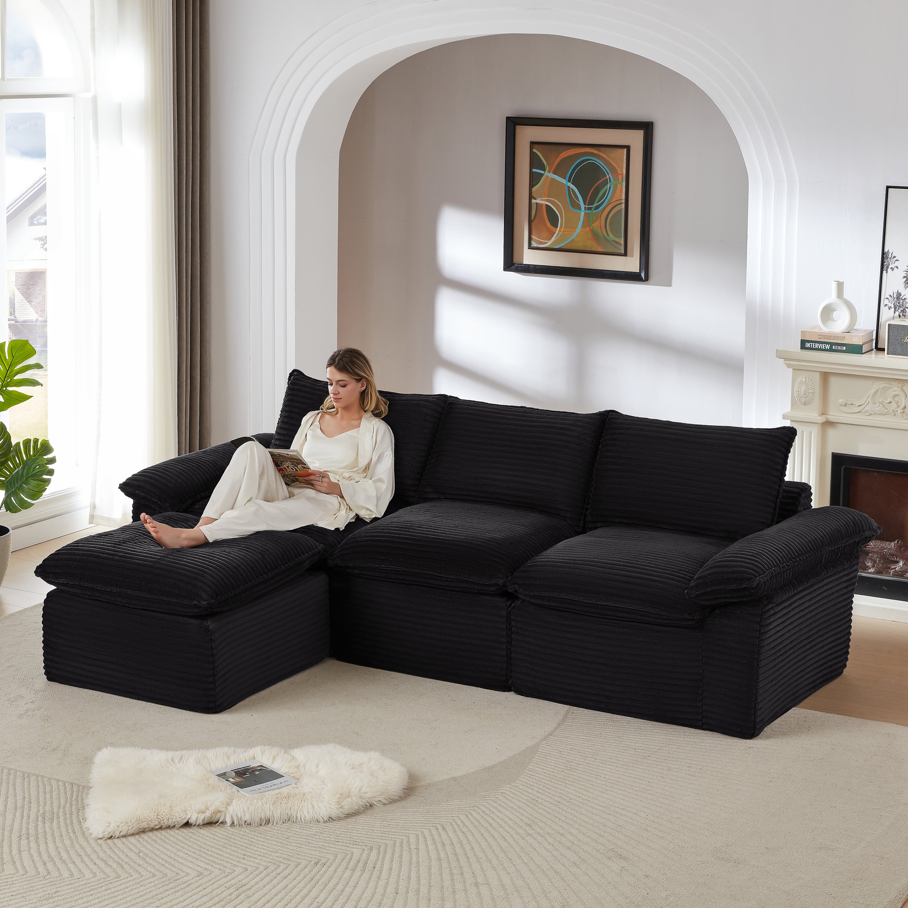 Modular corduroy sofa in black with chaise lounge, featured in a modern living room with a woman reading. Durable and stylish for contemporary homes.