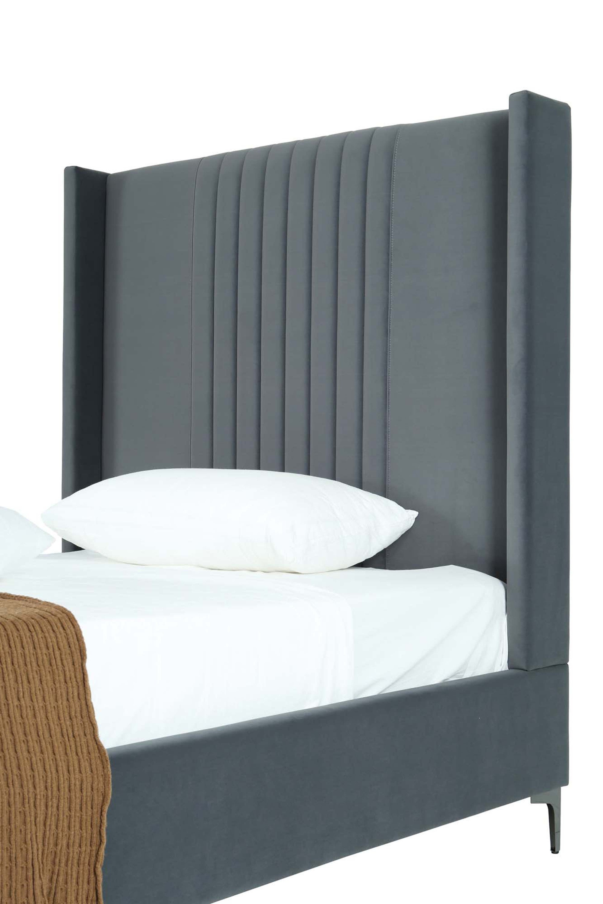 Close-up of gray velvet upholstered bed showing tall wingback headboard with vertical stitching and plush texture.
