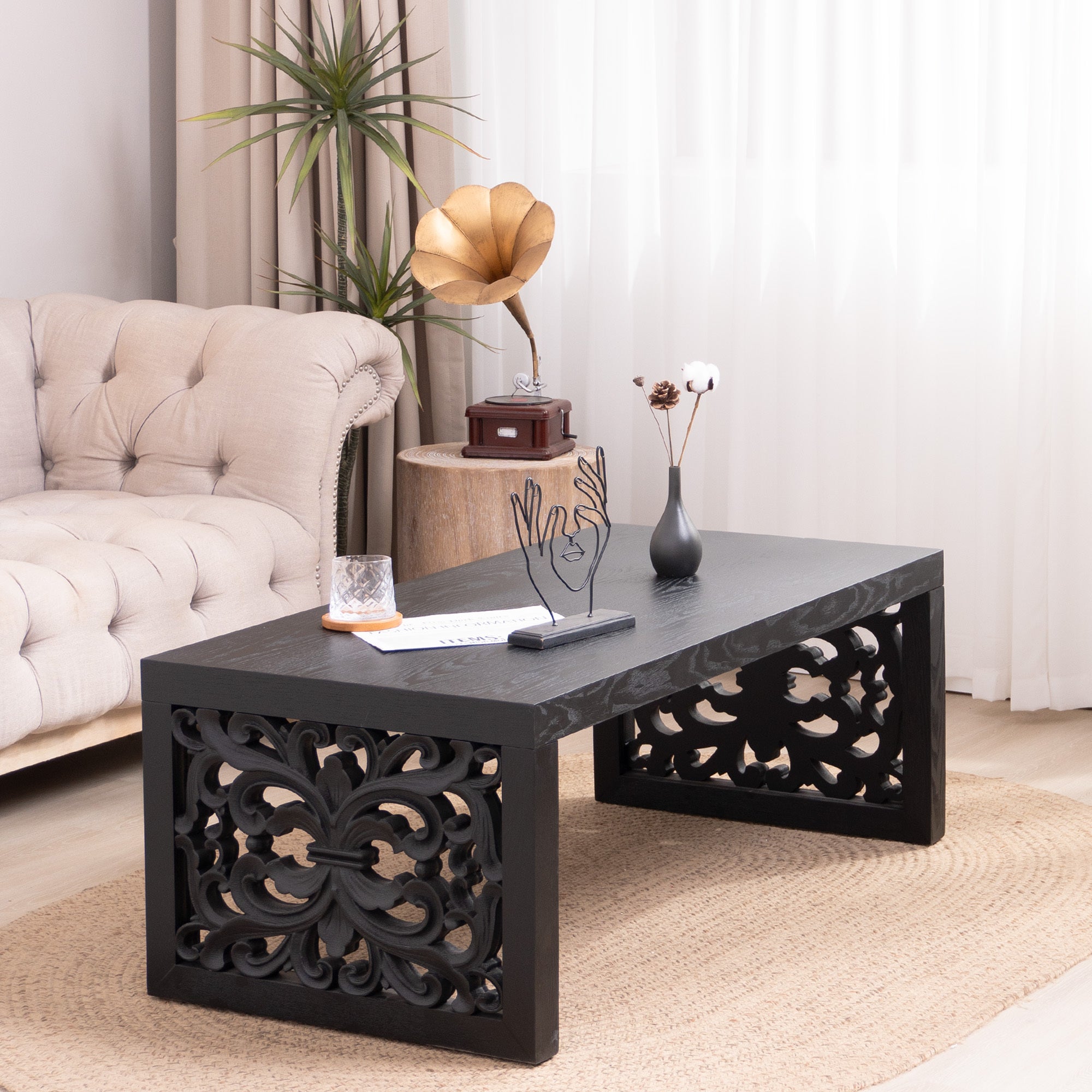 Handcrafted black carved wood coffee table styled in a modern living room, enhancing the decor with its ornate side panels.