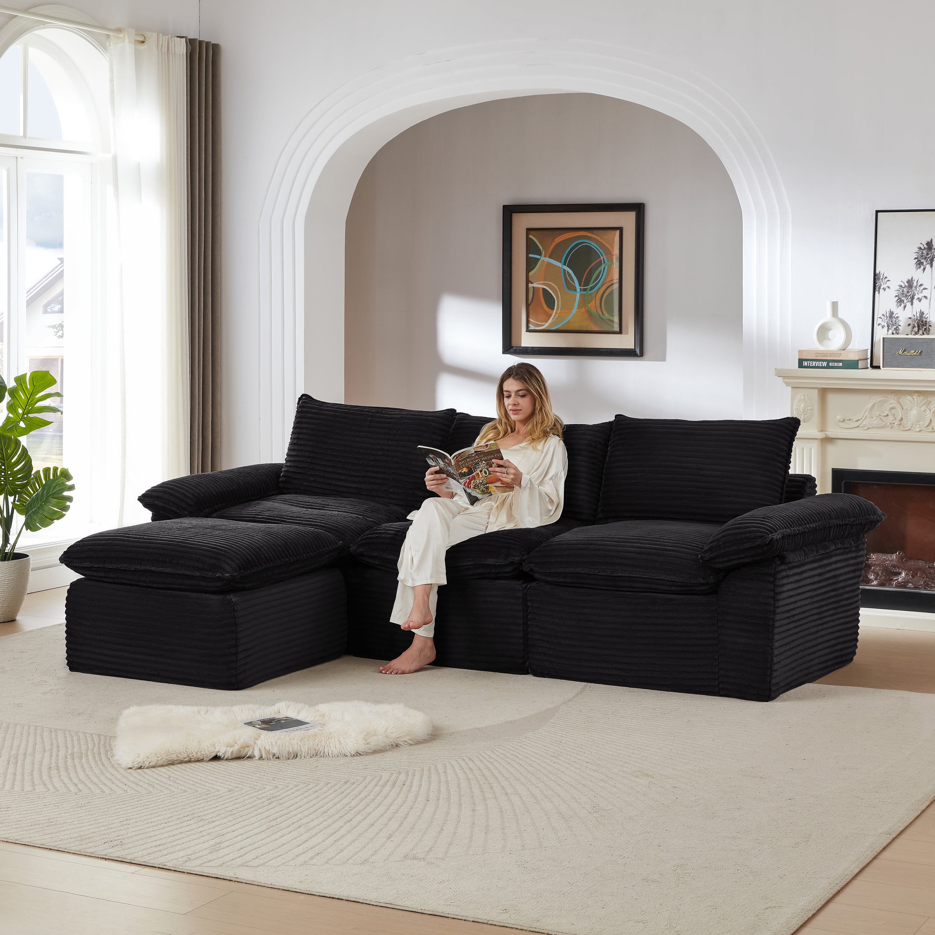 Black modular corduroy sofa with plush cushions and a woman reading, ideal for modern living rooms or apartments seeking comfort and flexibility.