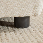 Close-up of the Evelyn sectional sofa leg, a sturdy black cylindrical base on a textured rug for stability and style.