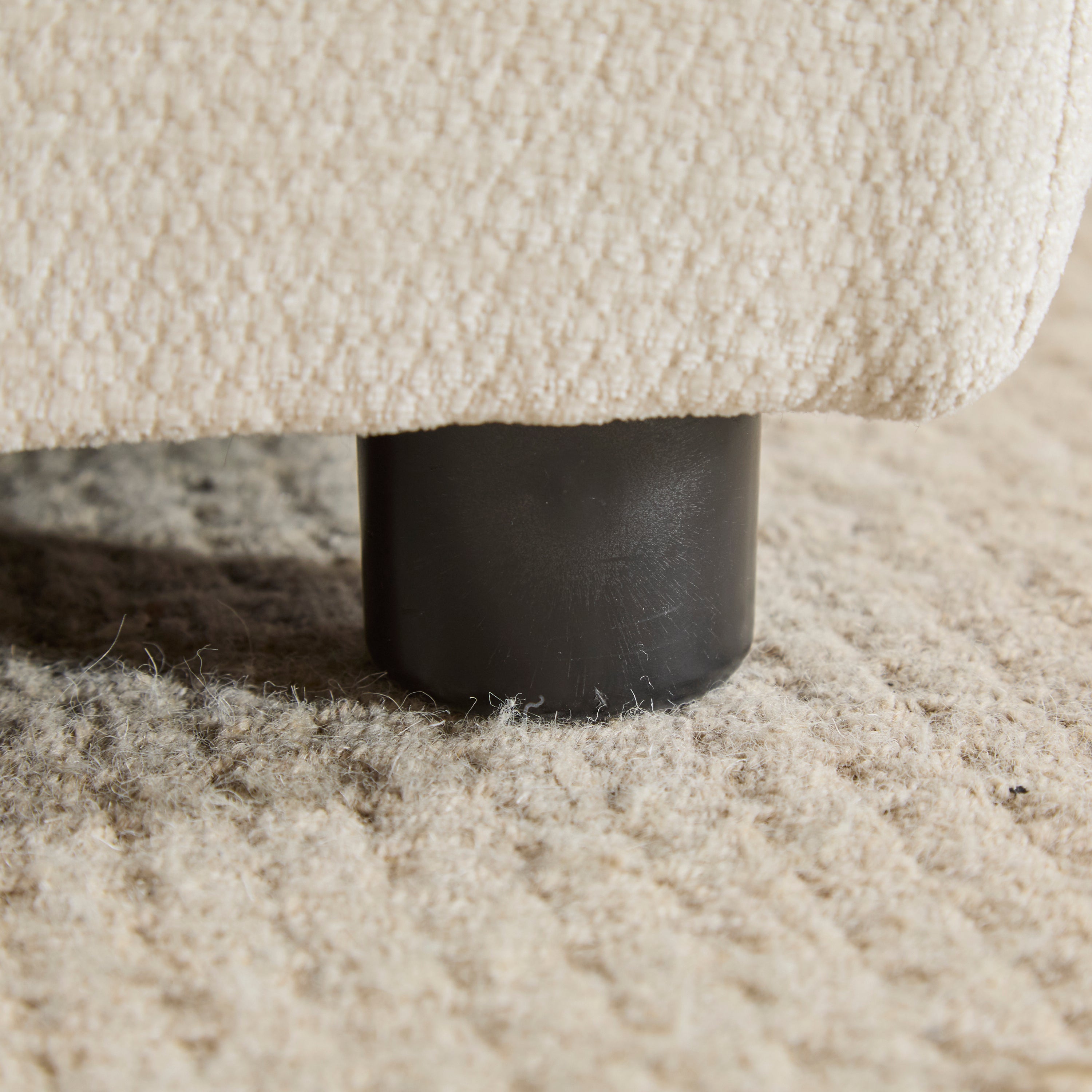 Close-up of the Evelyn sectional sofa leg, a sturdy black cylindrical base on a textured rug for stability and style.