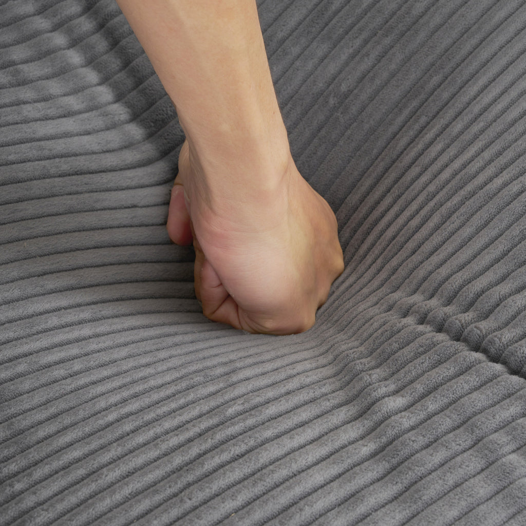 Hand pressing into plush cushion of dark grey modular sofa, demonstrating softness and resilience of corduroy upholstery.