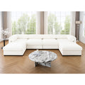 Large white modular U-shaped sectional sofa with cylindrical bolsters, set in a bright living room with marble table.