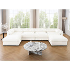 Large white modular U-shaped sectional sofa with cylindrical bolsters, set in a bright living room with marble table.