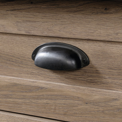 Detailed view of a black metal cup handle on the brown dresser drawer, highlighting its rustic and functional design.