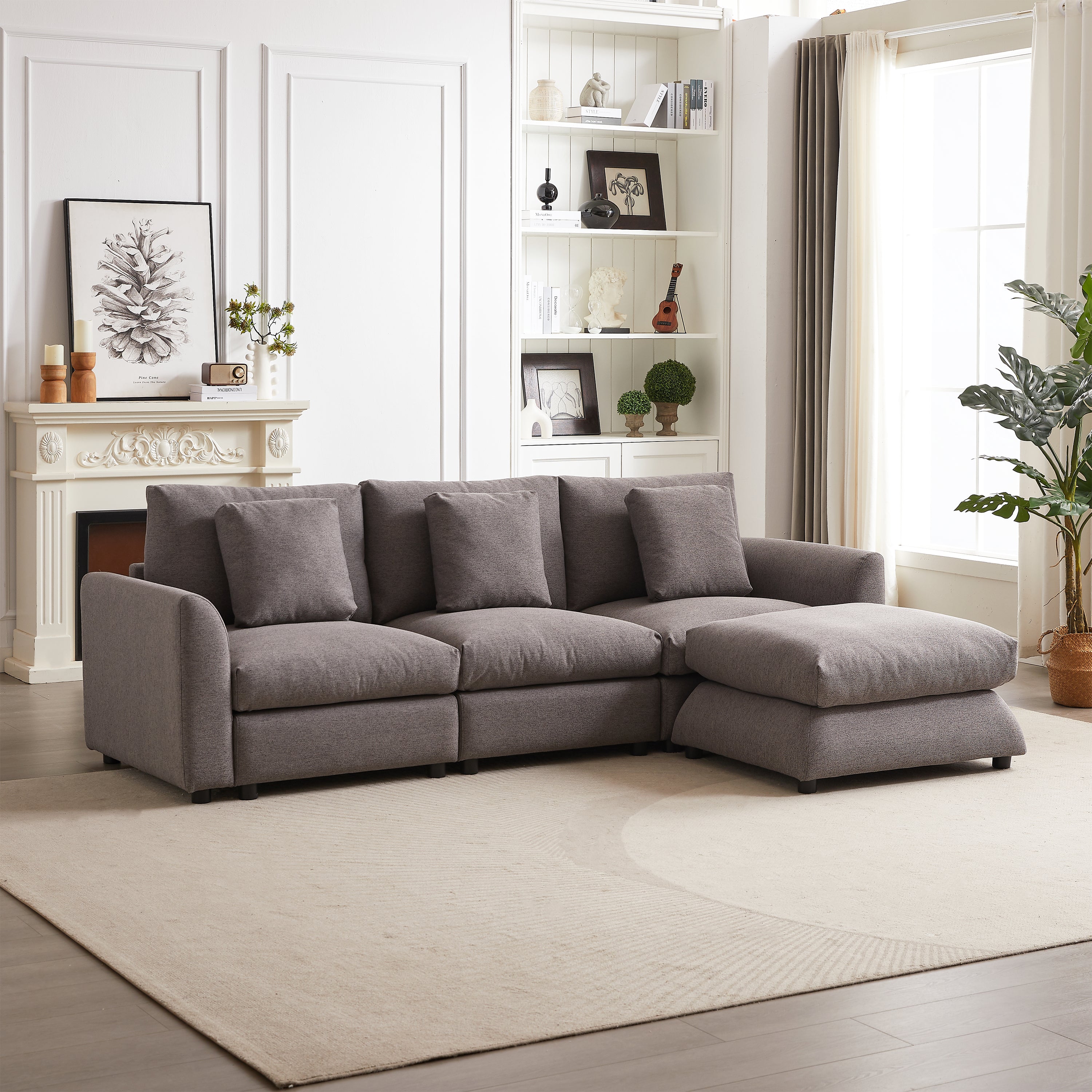 Gray upholstered modular sofa with ottoman in L-shape, placed in a spacious living room with neutral decor and natural light.
