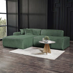 Left-facing green corduroy sectional sofa with a low-profile, modern design, set against a dark textured wall.
