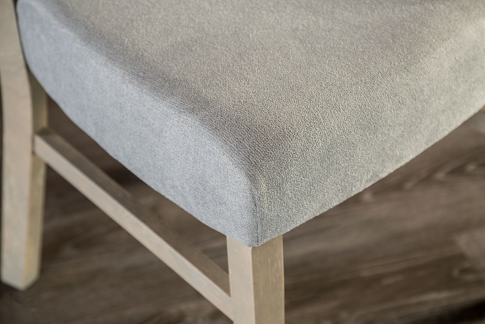 Close-up of gray padded seat on transitional dining chair, showcasing soft upholstery and sturdy wood frame.
