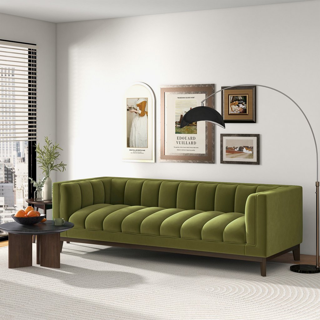 Mid-century modern sofa in olive green velvet with channel tufting and dark wood legs, set in a bright living room.