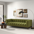 Mid-century modern sofa in olive green velvet with channel tufting and dark wood legs, set in a bright living room.