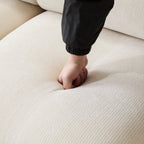 Hand pressing into the seat cushion of the Evelyn modular L shaped chenille sofa, showing its soft and resilient padding.